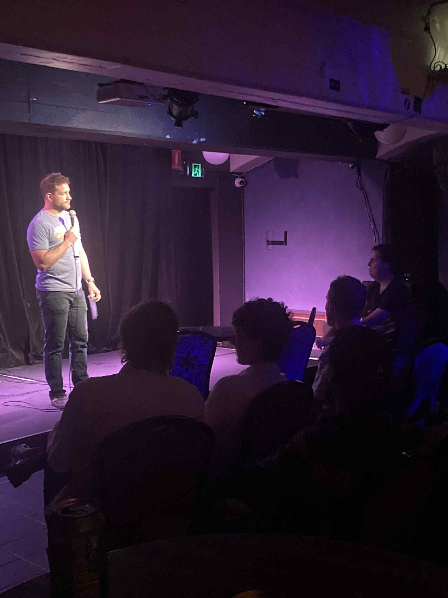 Russell Hartup is standing on stage with a microphone to his face talking to the crowd. In his hand is the list of performers and you can see the bulge from gorging himself over Christms.